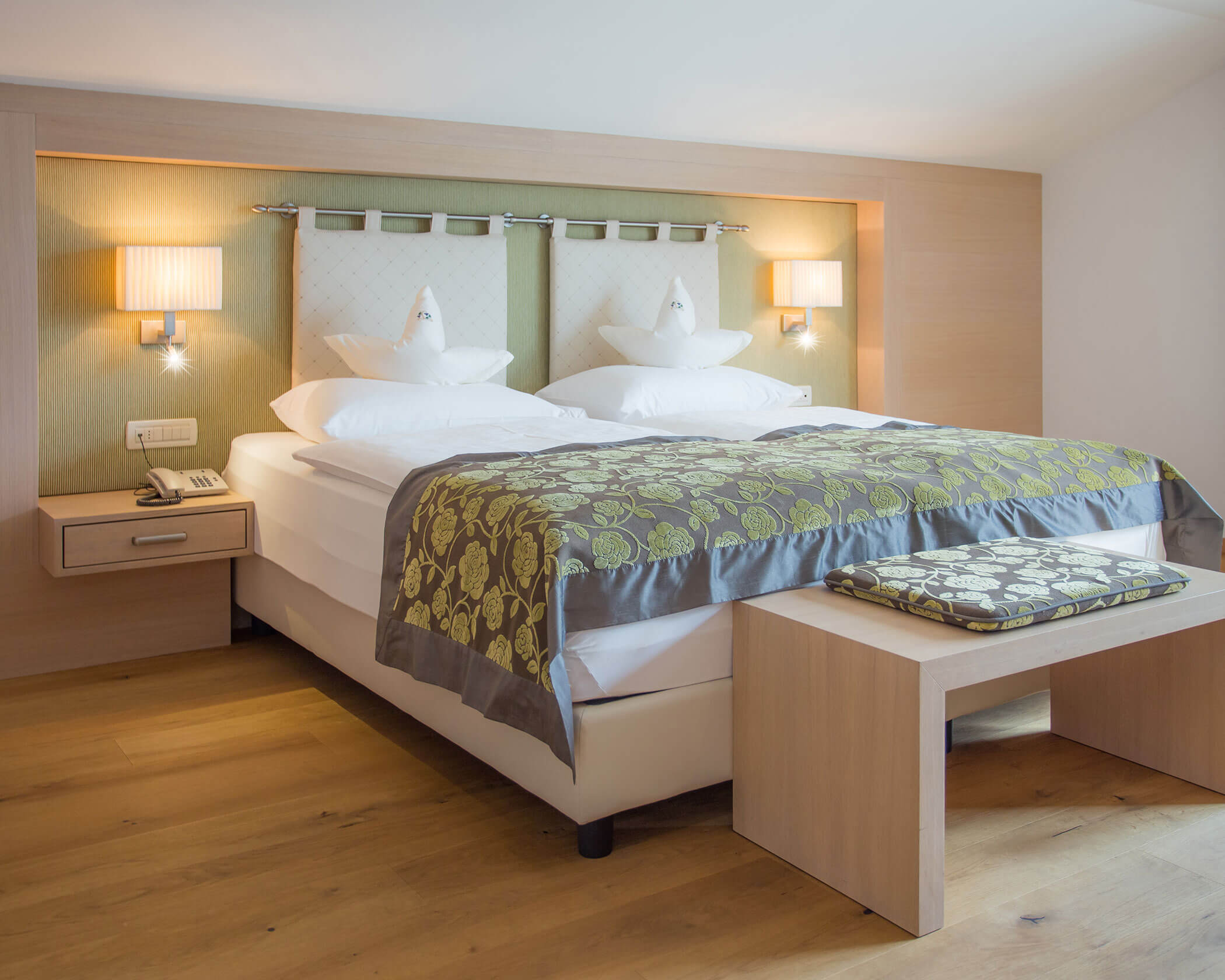 Modern hotel room with neatly made double bed, two lamps, bedside tables, and wooden flooring. - Hotel Lagrein