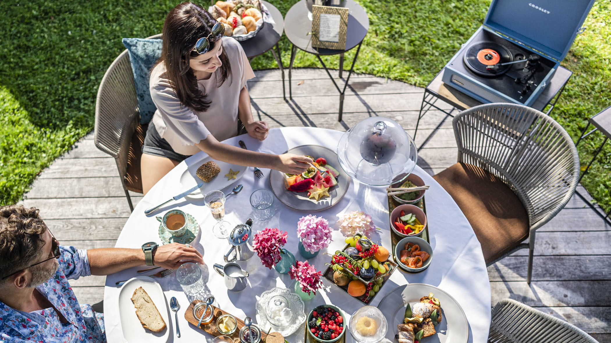 Frühstück im Freien im Garten mit Obst, Aufstrich, romantischer Tisch mit Plattenspieler, Croissant, Kuchen, Käse, Früchte