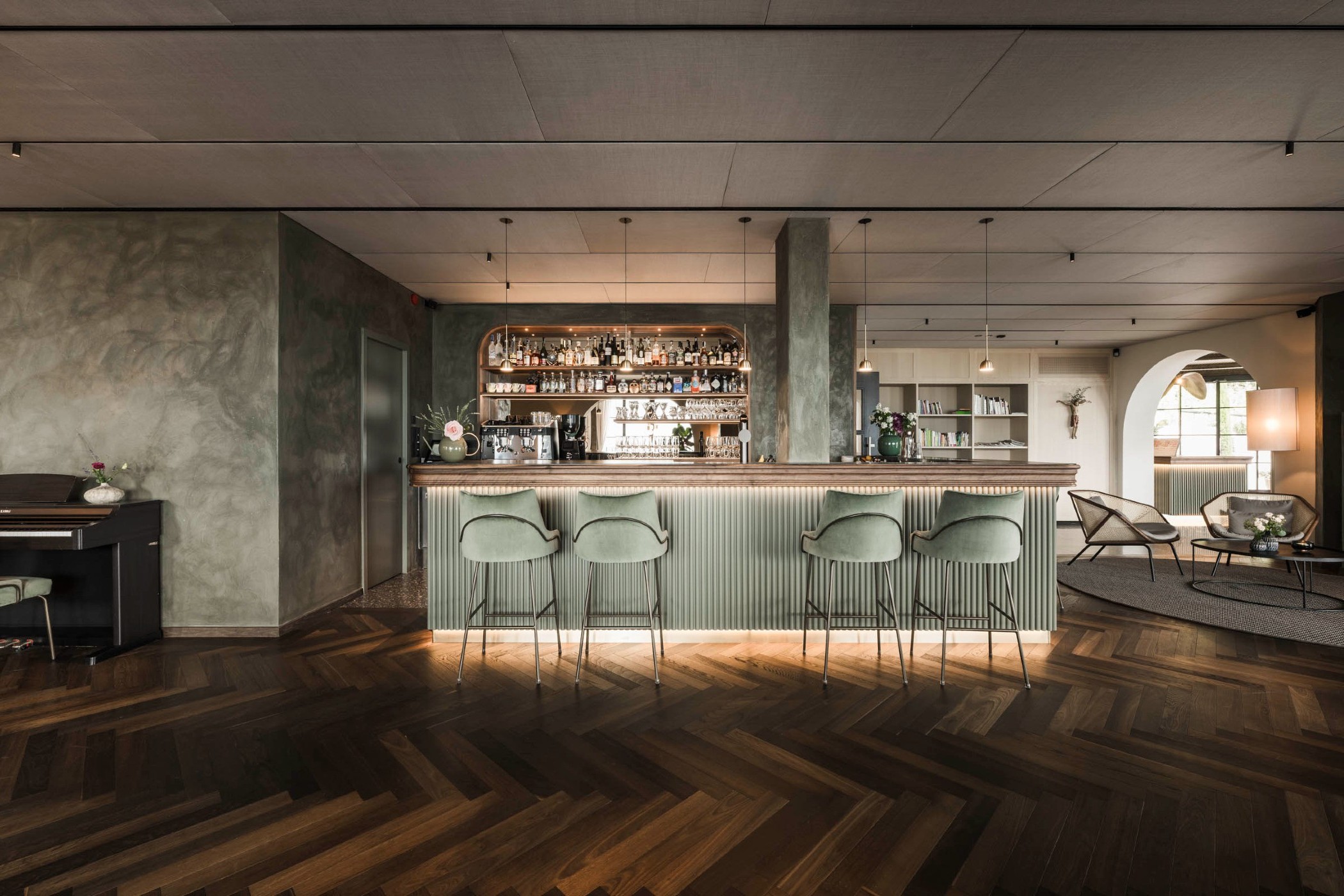 A stylish bar with shelves of liquor bottles, glassware, and a coffee machine behind a polished counter. - Hotel Lagrein