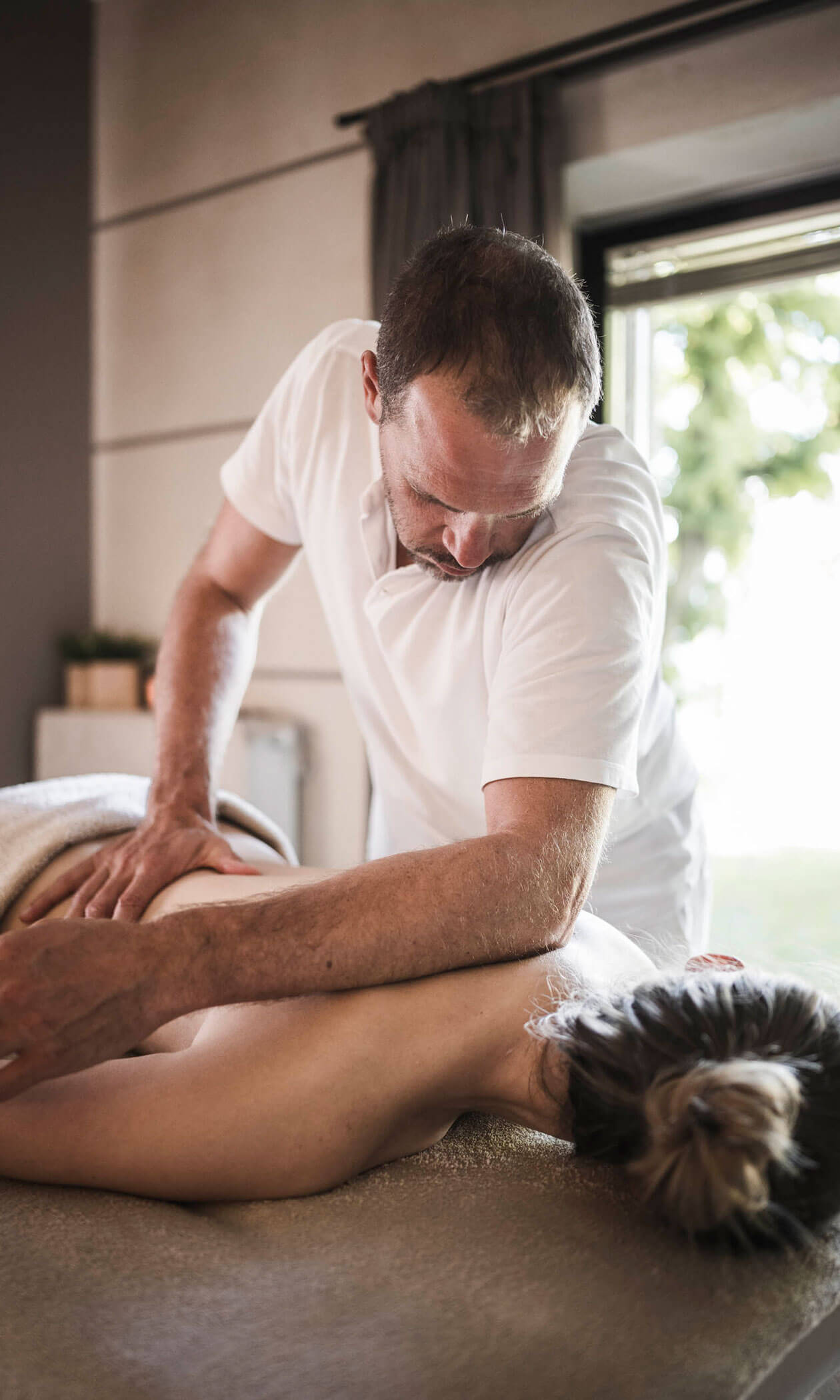 A man in a white shirt gives a massage to a person lying face down on a massage table. - Hotel Lagrein