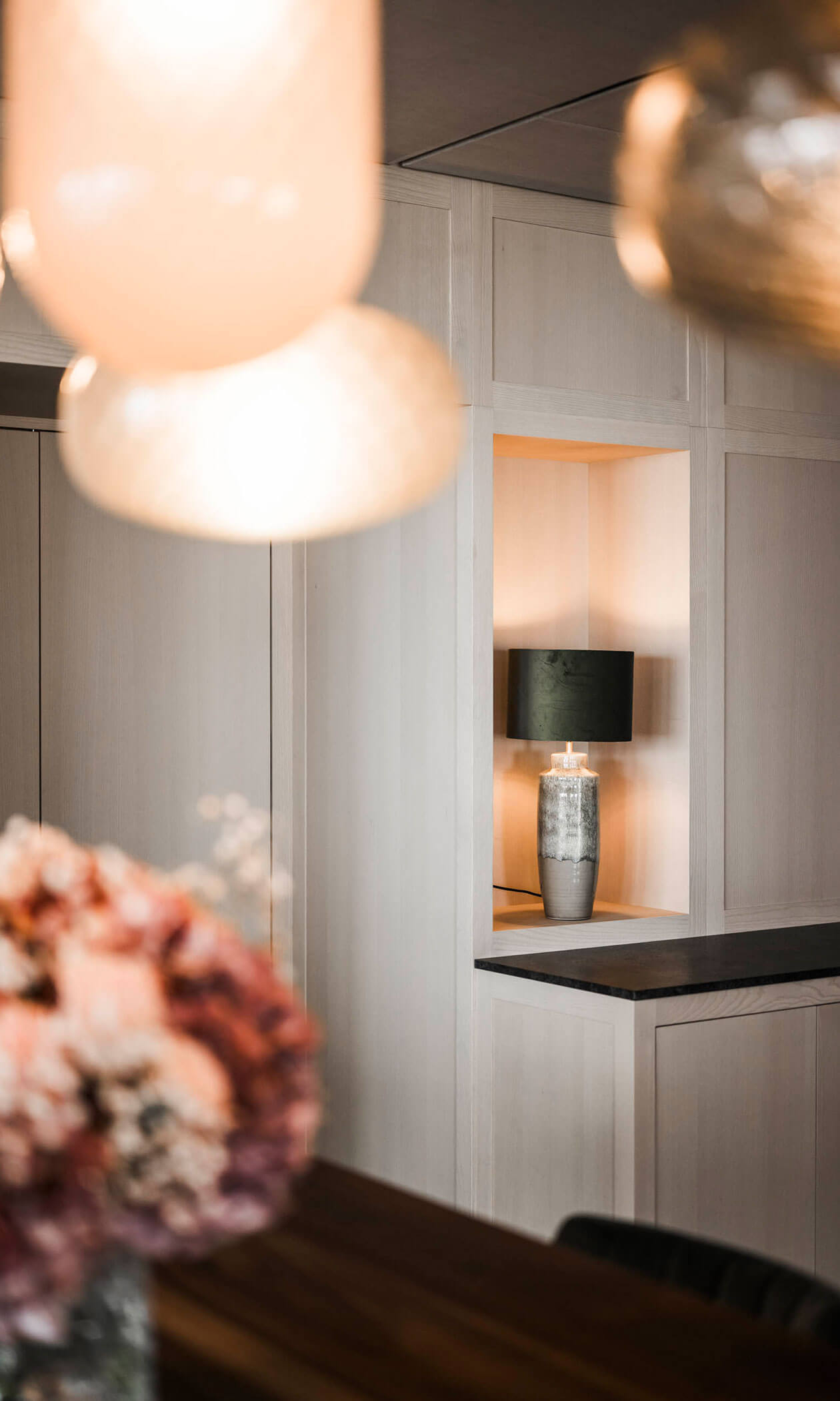 A modern interior with soft lighting, a vase of flowers, and a lamp on a shelf inset in a white wall. - Hotel Lagrein