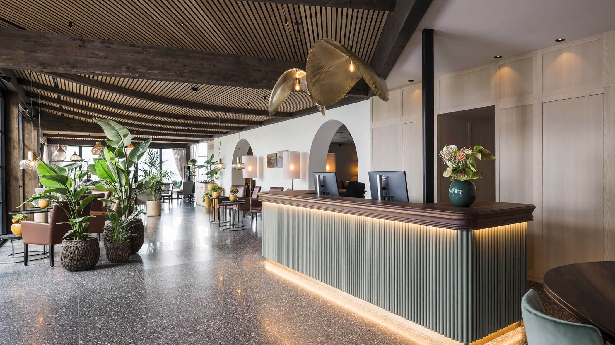 Modern hotel lobby with a stylish reception desk, indoor plants, and elegant lighting fixtures. - Hotel Lagrein