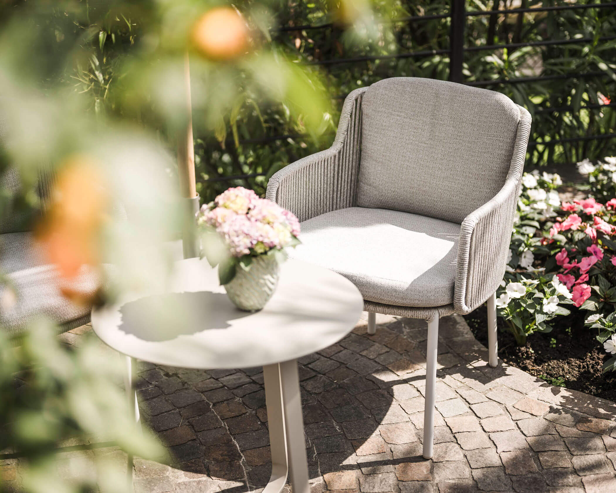 A cozy garden chair and table with a flower vase, surrounded by blooming flowers and greenery. - Hotel Lagrein