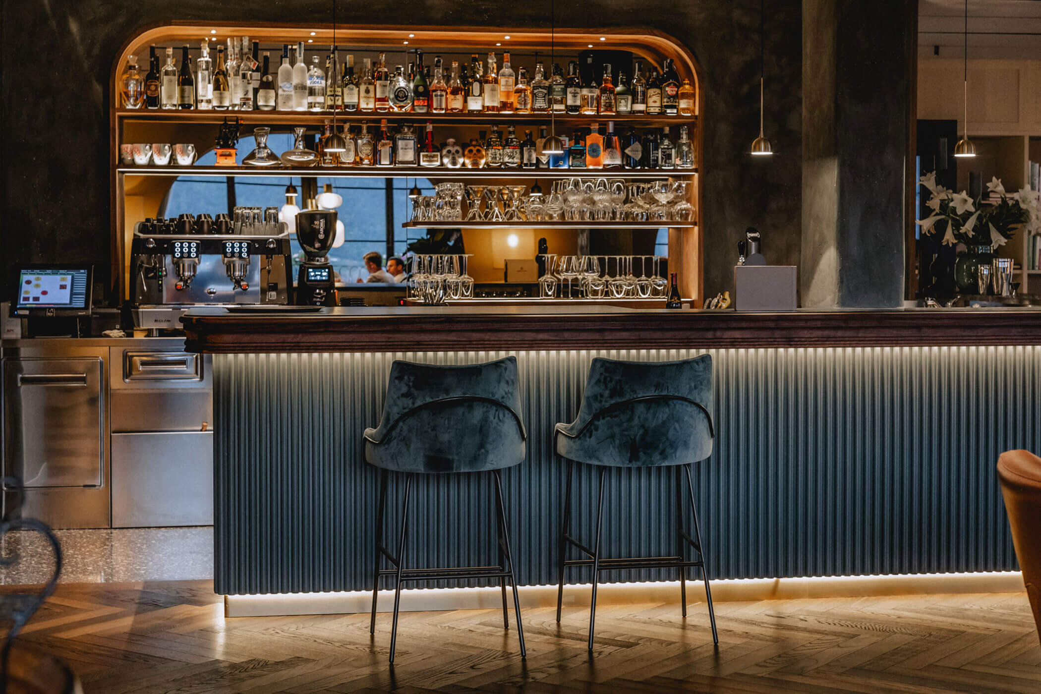 Chic bar with two velvet barstools, a stocked back bar, and warm, ambient lighting. - Hotel Lagrein