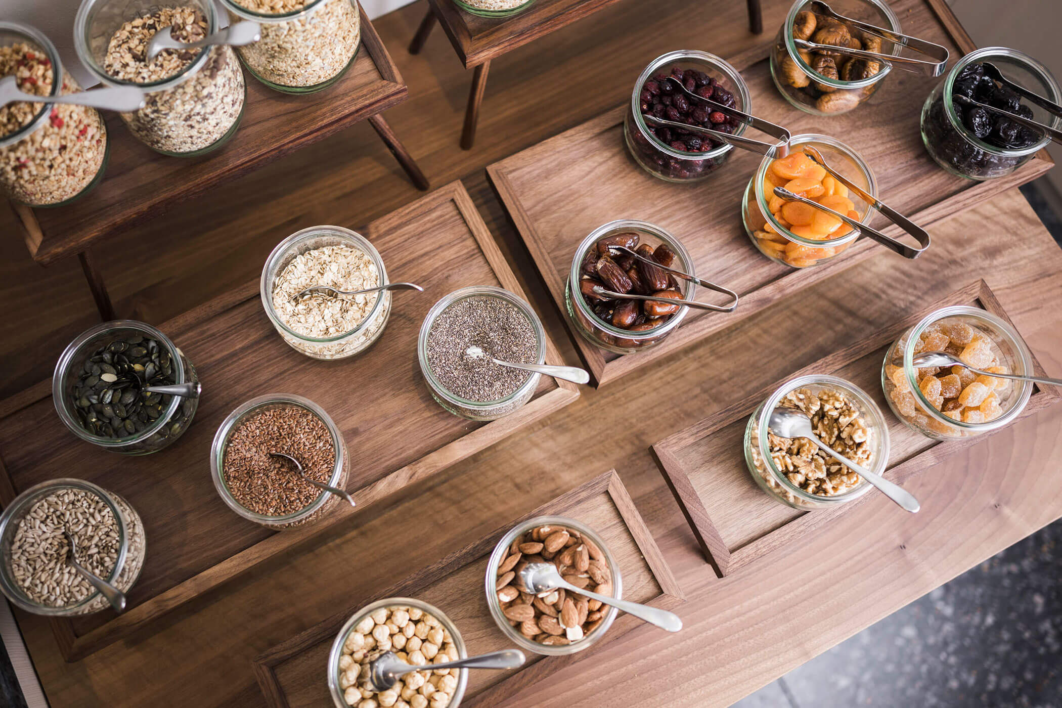 Jars of assorted dried fruits, nuts, and seeds arranged neatly on wooden trays with serving spoons. - Hotel Lagrein