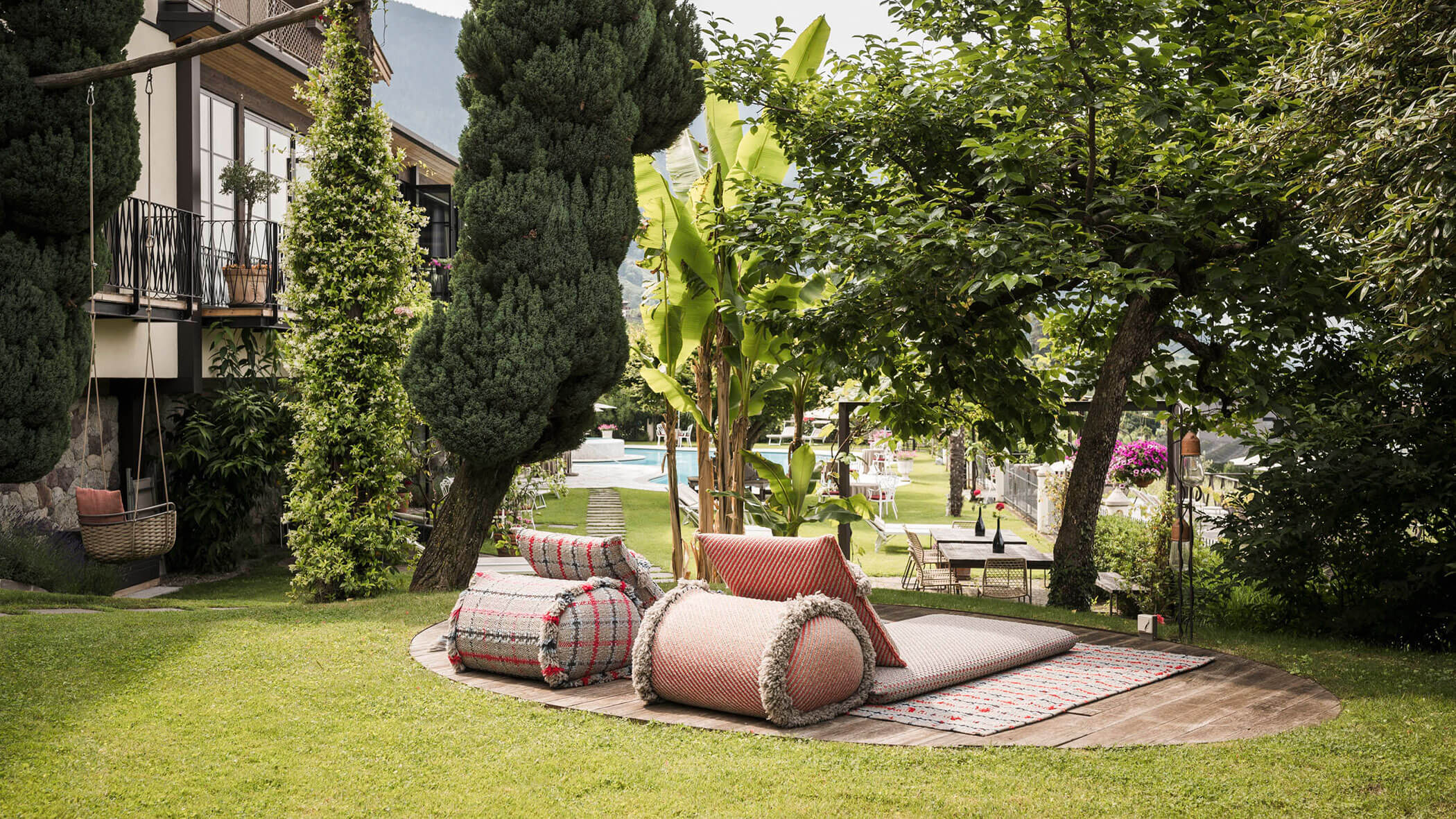 Outdoor lounge area with patterned cushions and rugs on grass, surrounded by lush trees and greenery. - Hotel Lagrein