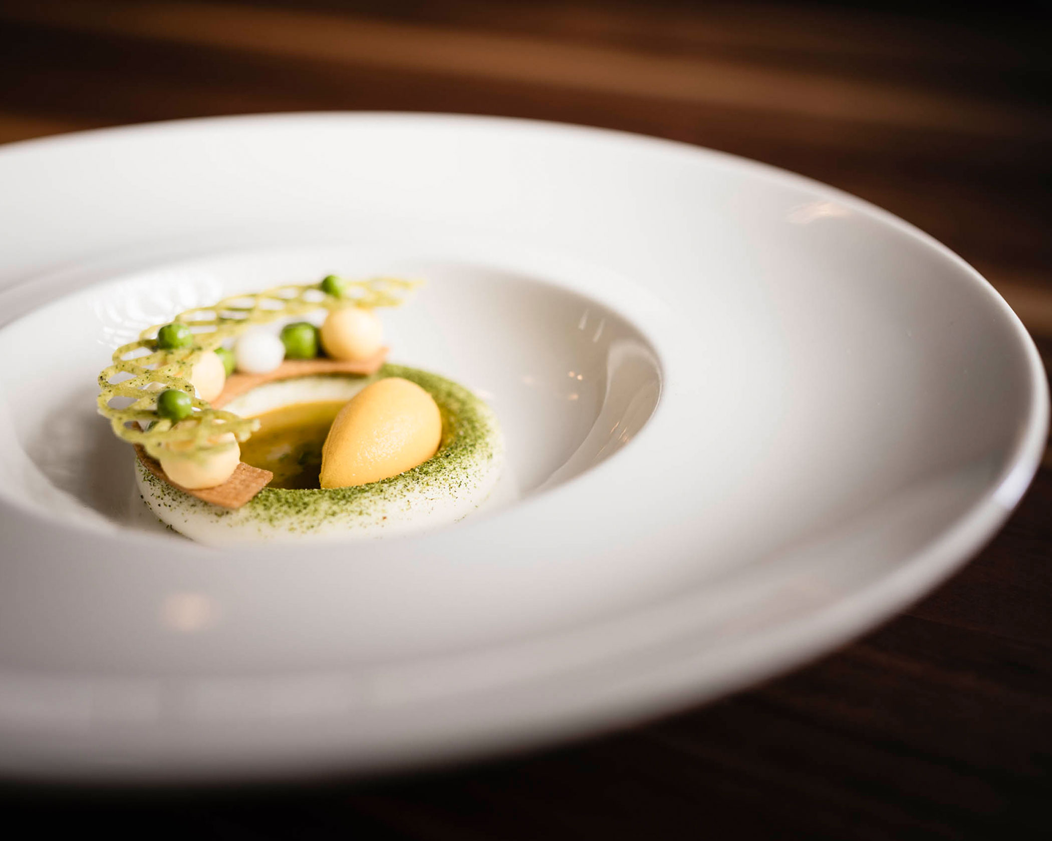 Elegant plated dessert with a yellow sorbet, mousse, and decorative garnish on a white dish. - Hotel Lagrein