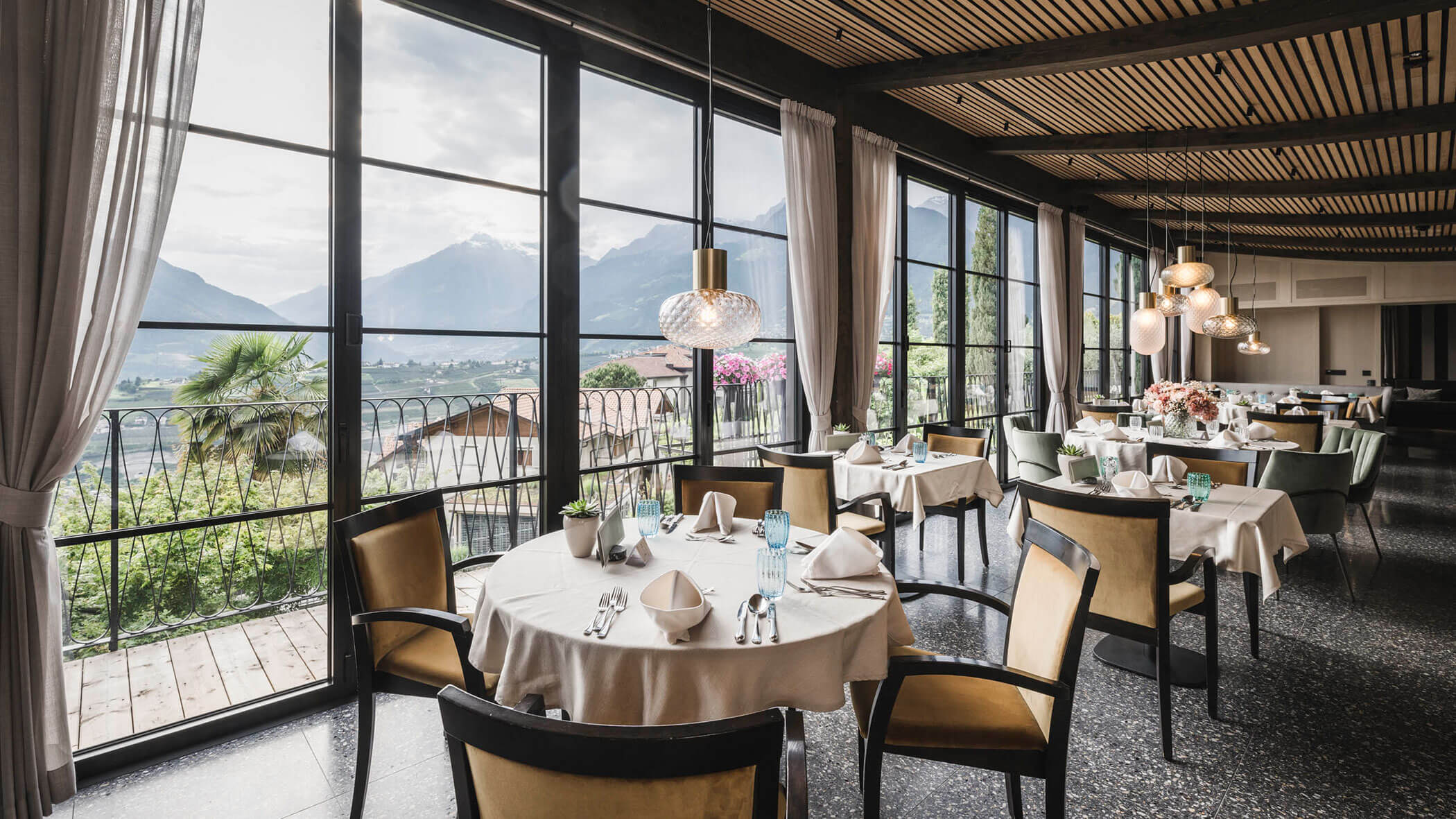 Elegant restaurant with set tables, large windows, and mountain views in the background. - Hotel Lagrein