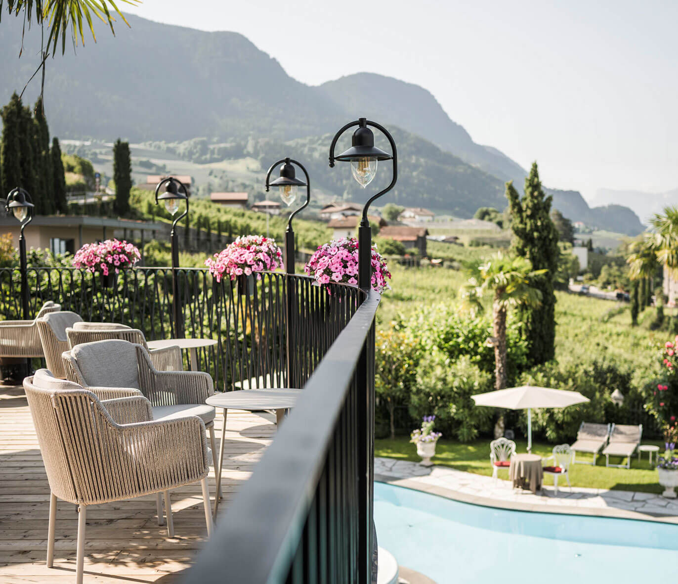 Outdoor terrace with chairs and flowers overlooks a pool and scenic mountains under a clear sky. - Hotel Lagrein