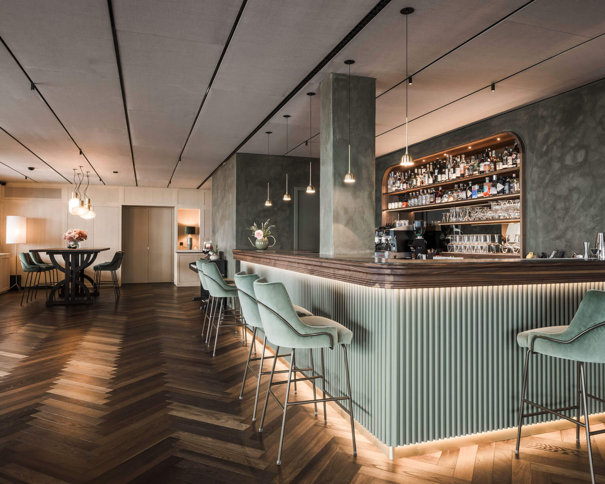 Modern bar with mint green chairs, wood herringbone floor, and shelves of bottles behind the counter. - Hotel Lagrein