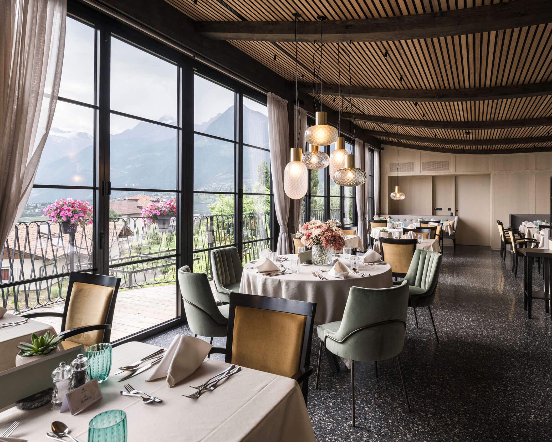 Elegant restaurant with round tables, modern lighting, and large windows overlooking mountains and flowers. - Hotel Lagrein