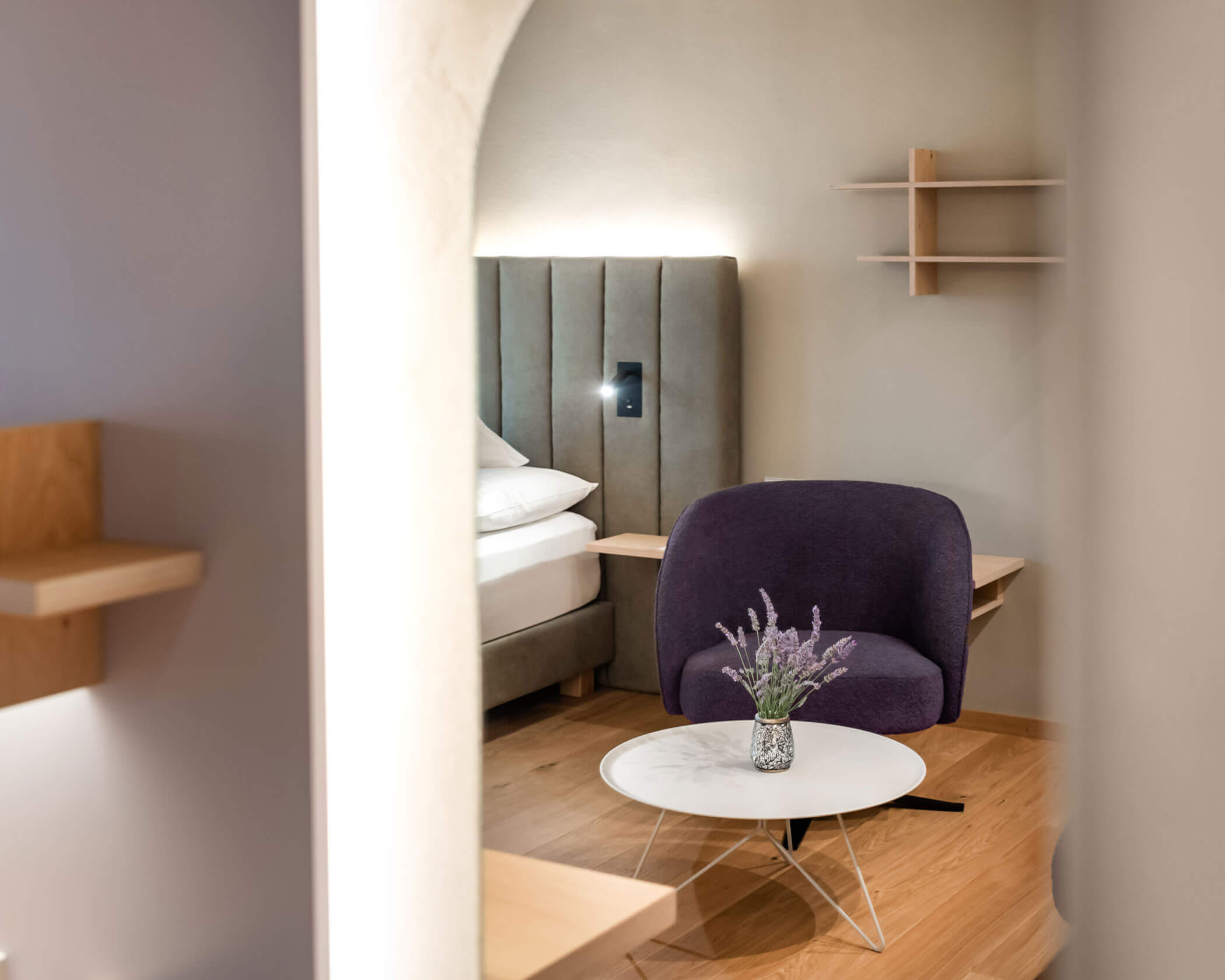 Modern bedroom with a purple chair, round white table, and lavender vase, viewed through an arched doorway. - Hotel Lagrein