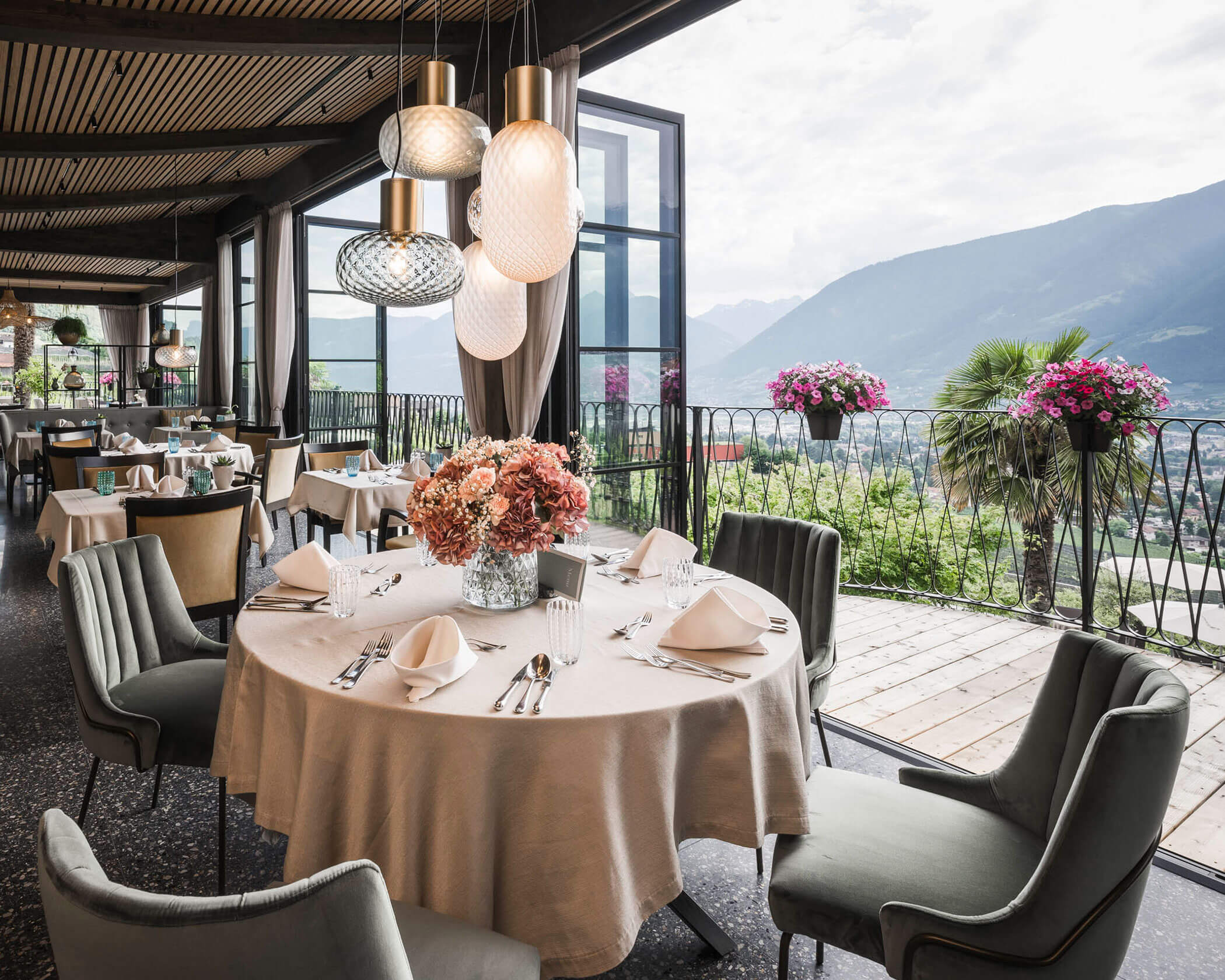 Elegant restaurant with set tables, floral centerpieces, and mountain views through large open windows. - Hotel Lagrein