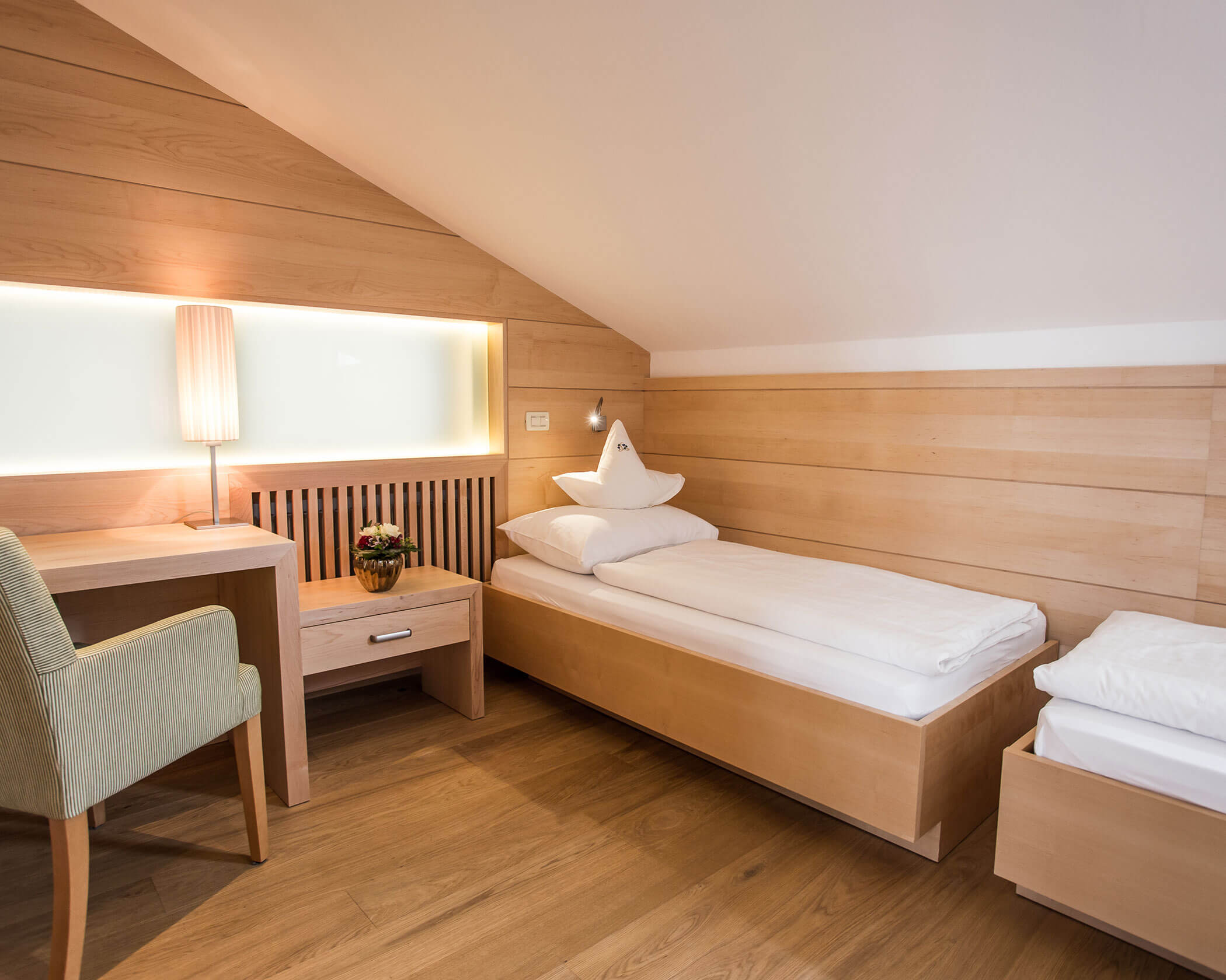 Minimalist hotel room with a single bed, desk, chair, lamp, and wooden paneling on the walls and floor. - Hotel Lagrein