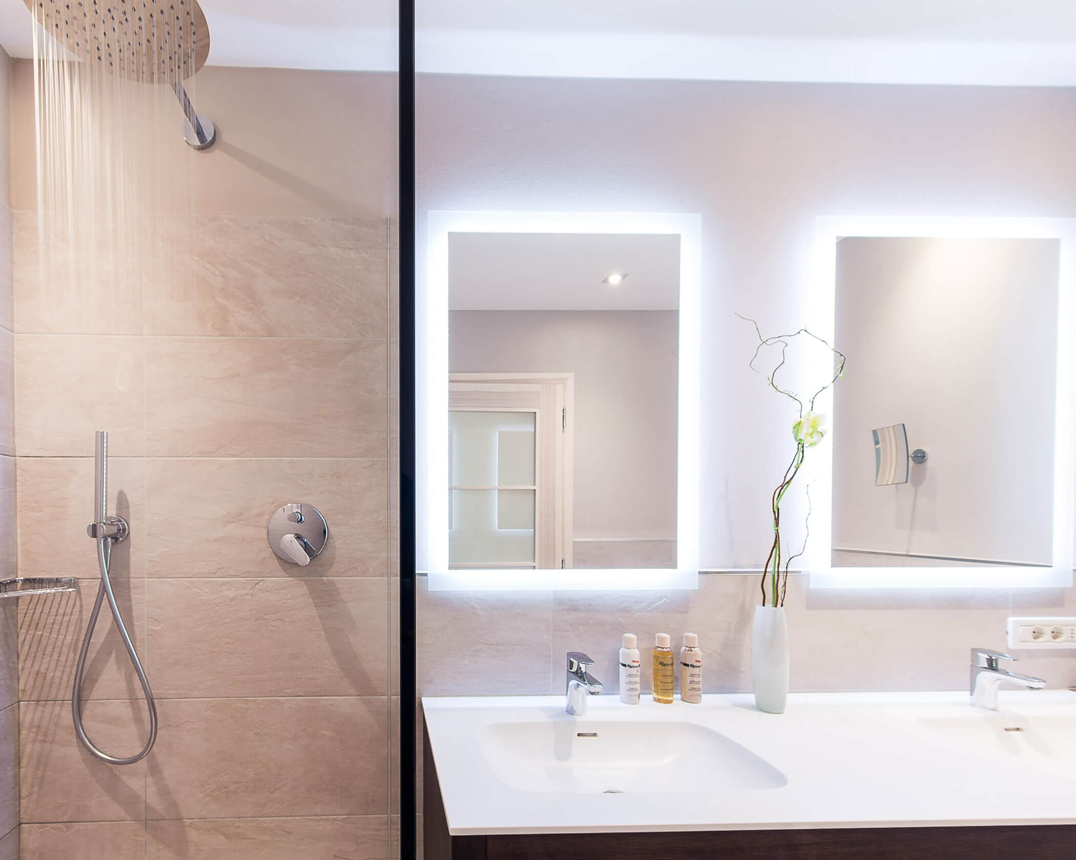 Modern bathroom with a rainfall shower, double sink, backlit mirrors, and minimalistic decor. - Hotel Lagrein