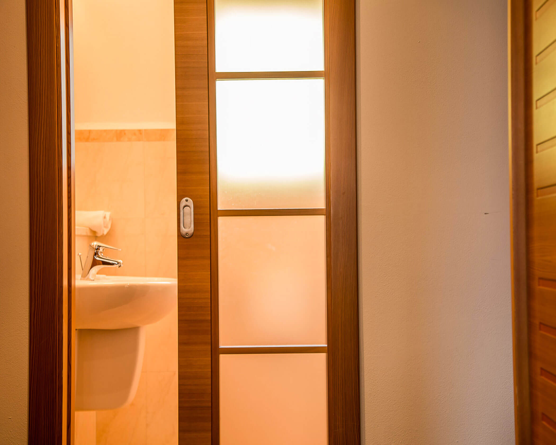 Sliding wooden door partially open to a bathroom with a white sink and towel visible. - Hotel Lagrein