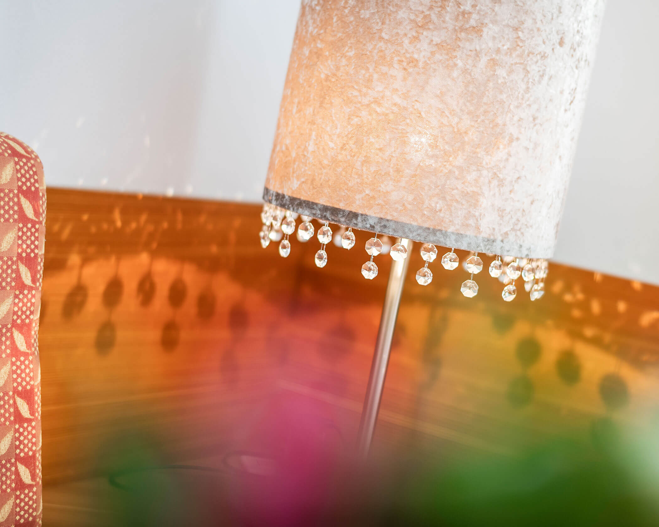 A lit lamp with a beaded edge casting reflections, next to a patterned chair and blurred greenery. - Hotel Lagrein