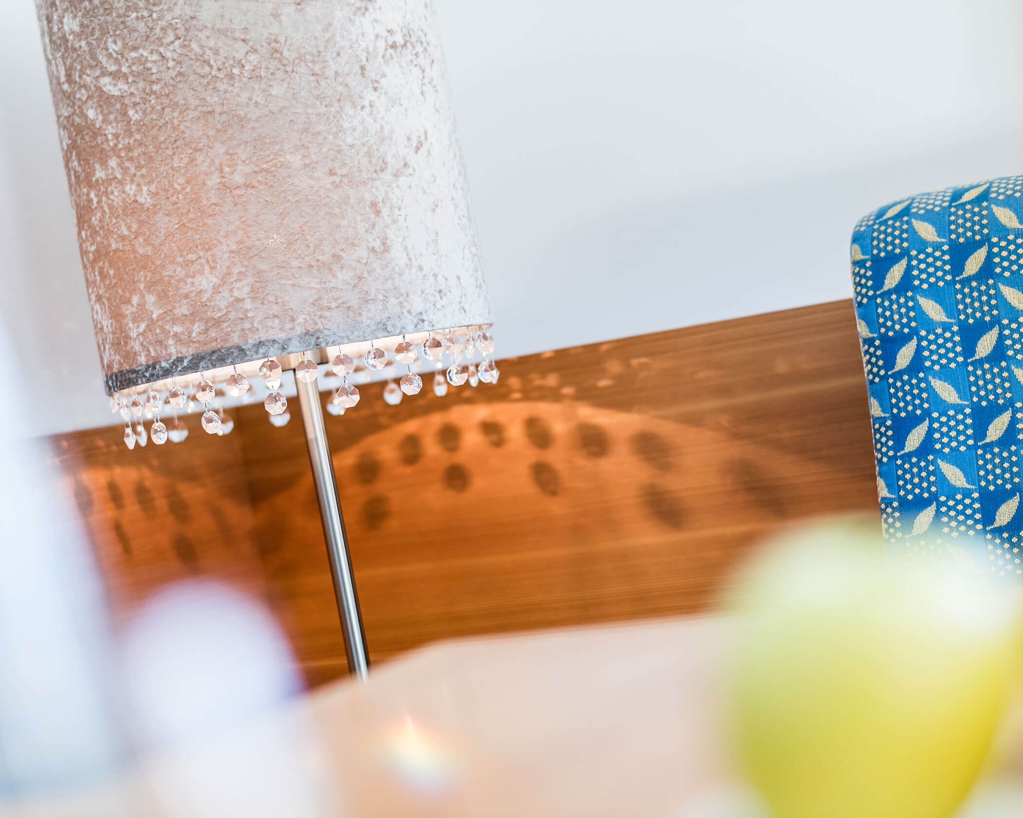 Lamp with crystal accents casting light patterns on a wooden wall, next to a blue chair with leaf prints. - Hotel Lagrein