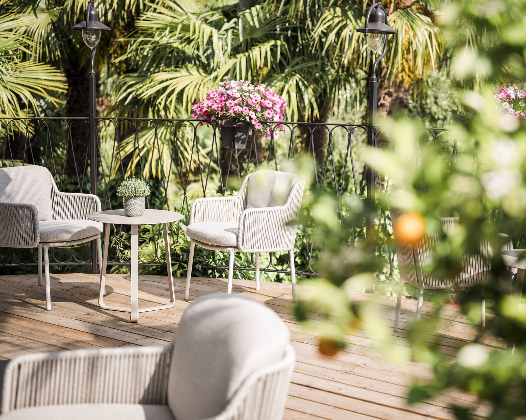 Outdoor patio with white chairs, a small table, potted plants, and lush greenery in the background. - Hotel Lagrein