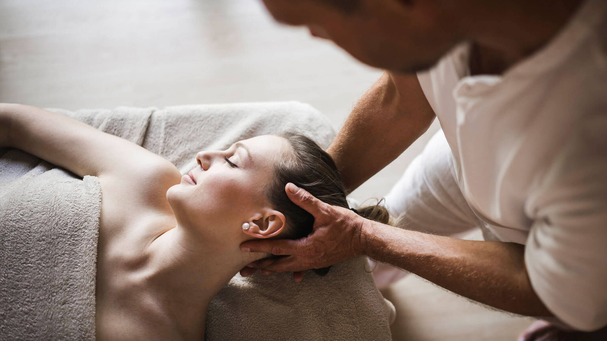 Person receiving a relaxing massage while lying on a towel, with a therapist gently holding their head. - Hotel Lagrein