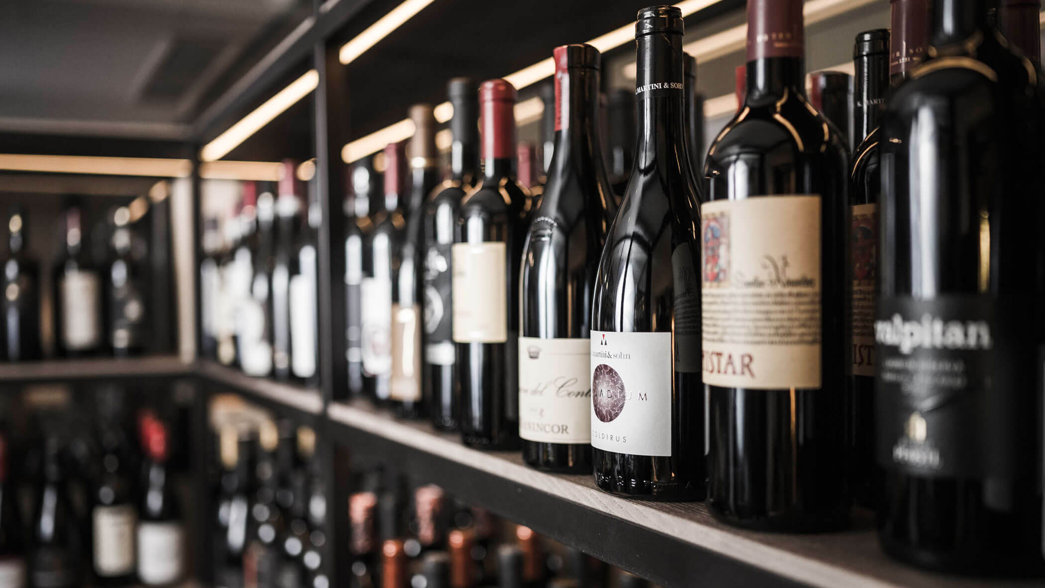 Close-up of assorted wine bottles lined up on shelves in a wine shop or cellar. - Hotel Lagrein