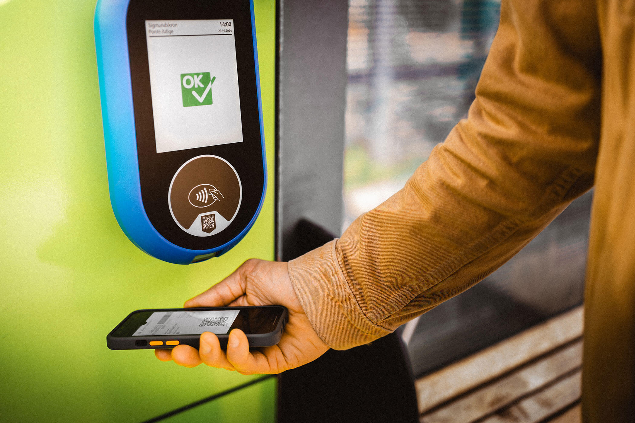 Person holds a phone with a QR code under a contactless ticket scanner with an OK checkmark display. - Hotel Lagrein