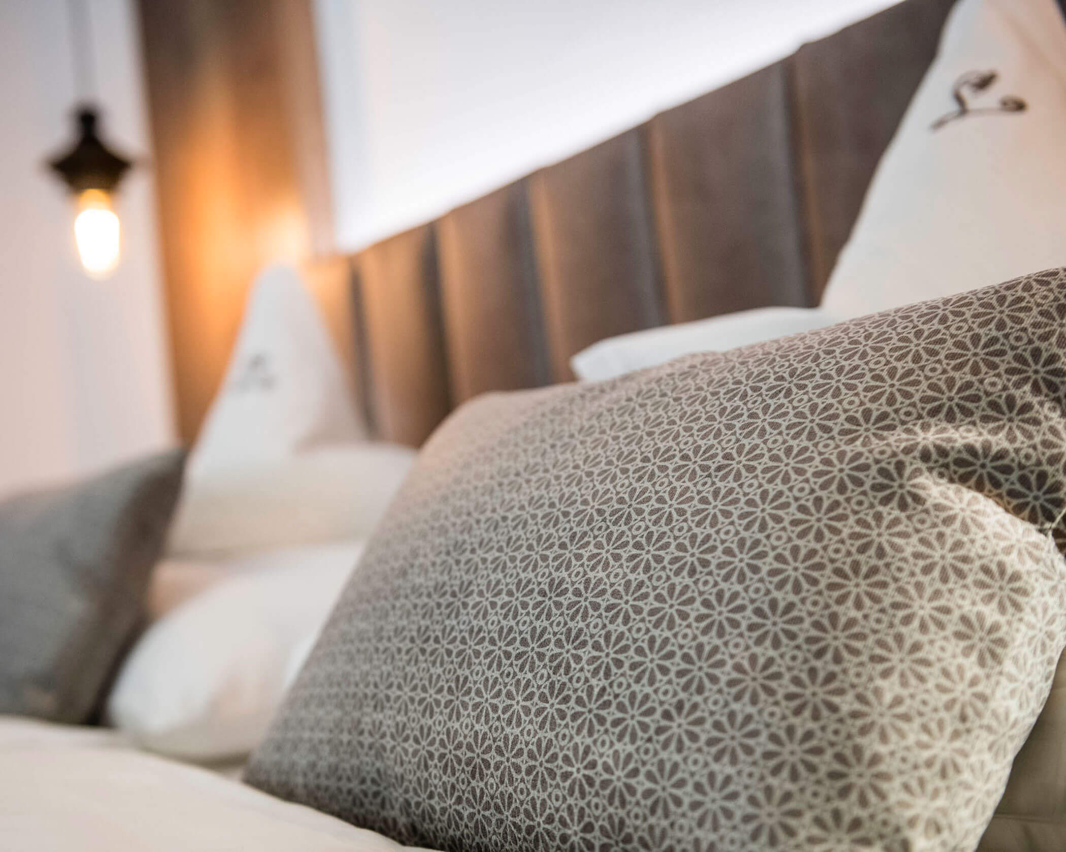 Close-up of a patterned pillow on a neatly made bed with white pillows and a headboard in the background. - Hotel Lagrein